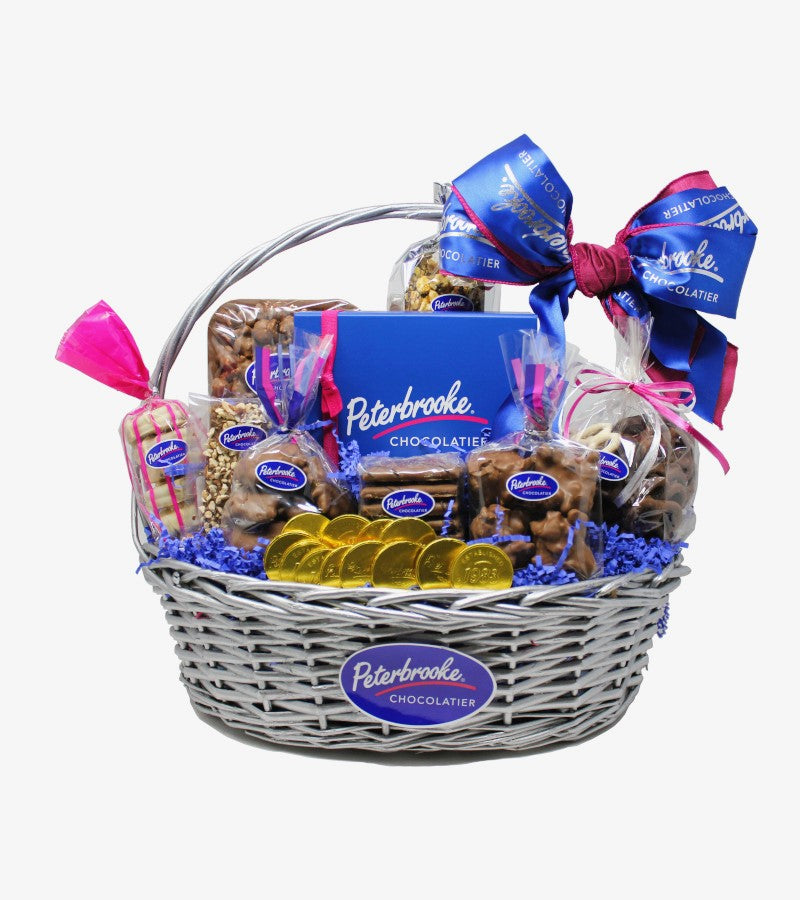 A Signature Chocolate Gift Basket containing various chocolate covered treats including popcorn, caramel corn, assorted chocolates, pretzels, and cookies, all arranged in a wicker basket with blue and pink ribbons.