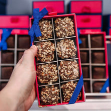 Hand holding an open box of english toffee with a blue bow