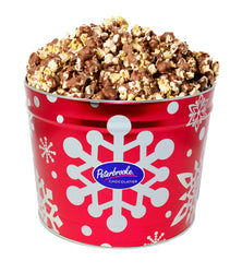 A red holiday tin with white snowflake designs, filled with milk chocolate covered popcorn.
